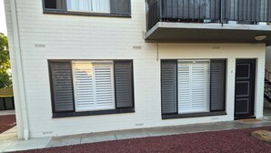A two-story building with white brick exterior, large windows with shutters, and a small balcony.