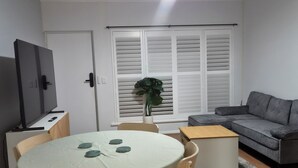 A modern living room with a round table, chairs, a sofa, a TV, and a ceiling fan.