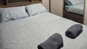 A neatly made bed with striped bedding, a wooden headboard, and a large mirror reflecting the room.