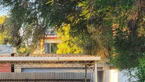 A covered outdoor area with a metal fence, concrete floor, and a building in the background.