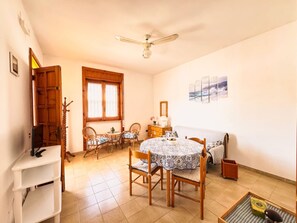 Ein Zimmer mit Esstisch, Stühlen, Deckenventilator, Fenster und Bildern an der Wand.