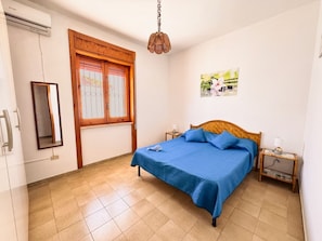 Ein Schlafzimmer mit einem Bett, einem Fenster, einem Spiegel, einer Wandklimaanlage und einem Bild.