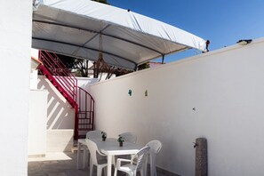 Eine Terrasse mit einem weißen Tisch und Stühlen, einer roten Treppe und einer weißen Wand mit einer kleinen Pflanze.