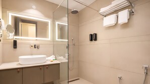 Ett modernt badrum med en duschavdelning med glasväggar, en stor spegel, en vit handfat och en toalett.