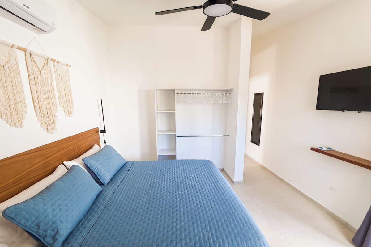 A bedroom with a bed, a ceiling fan, a TV, and a wardrobe.