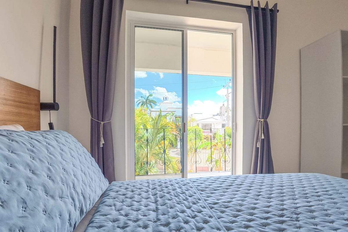A bedroom with a bed, curtains, and a view through a sliding glass door.