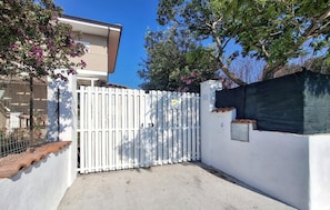A gated entrance to a building with a white wall, a tiled roof, and a metal gate. - 1 bedroom cozy apartment in Ricadi (Ricadi)