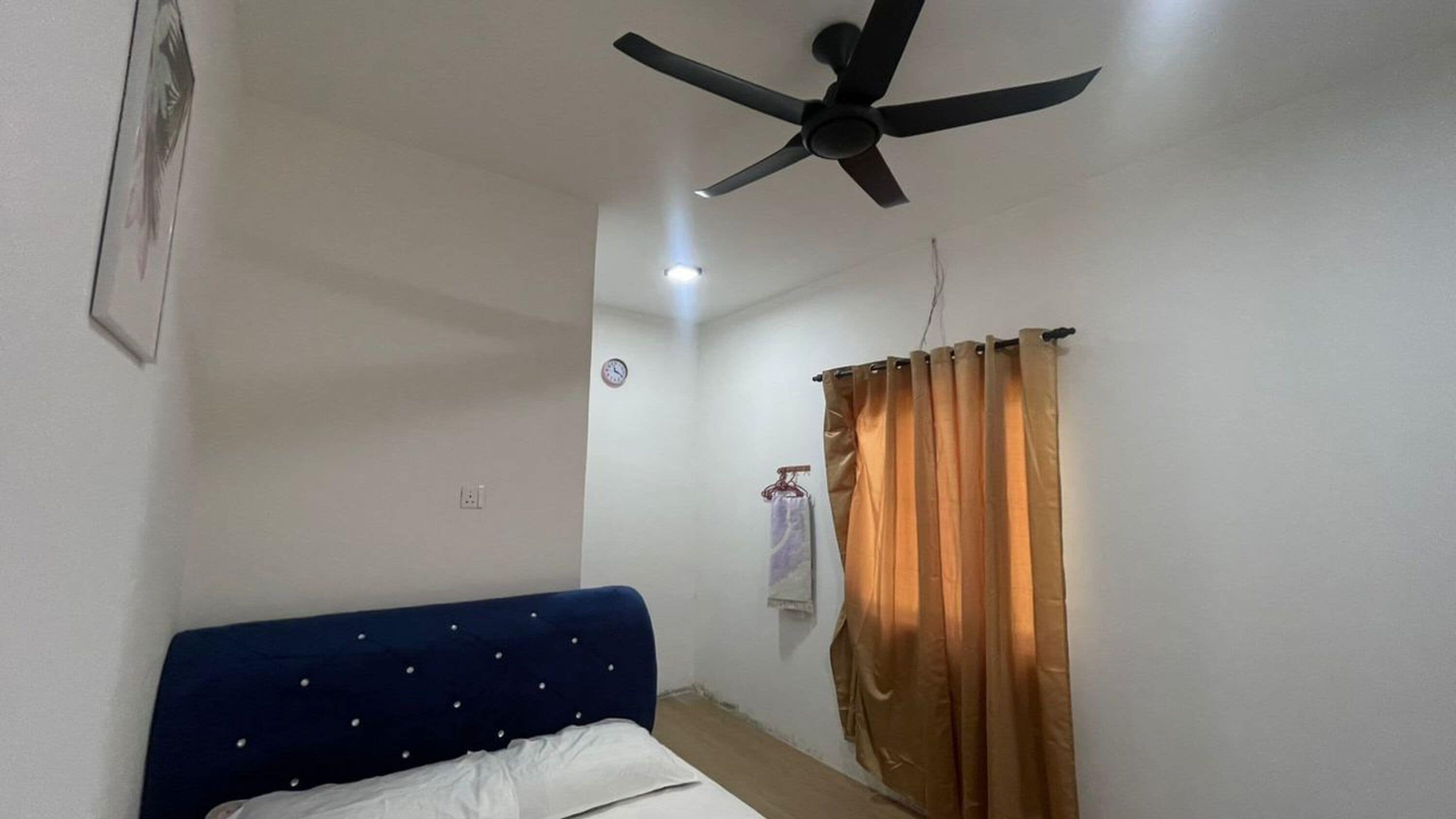 A bedroom with a bed, a ceiling fan, a clock, and a window with curtains.