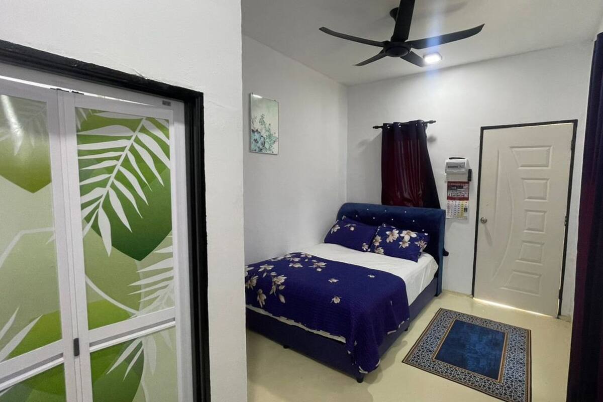 Un dormitorio con cama, ventilador de techo, una puerta y una ventana con cortinas.