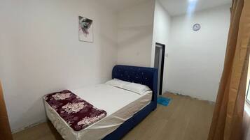 A bedroom with a bed, a door, a wall clock, and a framed picture.
