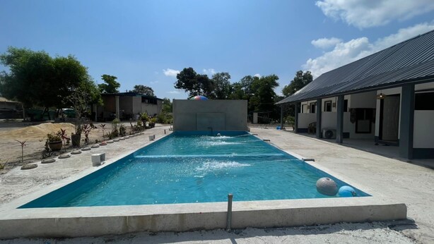 A rectangular swimming pool with a concrete deck, surrounded by potted plants and a building with a metal roof. - OYO 91303 Chalet Awie (Setiu)