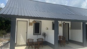 A building with a metal roof, a white door, and a small porch area with wooden chairs and a fan. - OYO 91303 Chalet Awie (Setiu)