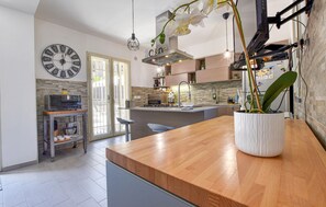 A modern kitchen with a wooden countertop, a large clock, and a potted orchid. - Nice home in san giovanni la punta (San Giovanni La Punta)