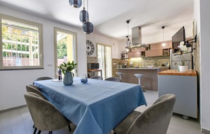 A dining area with a table set for four, a kitchen in the background, and a clock on the wall. - Nice home in san giovanni la punta (San Giovanni La Punta)