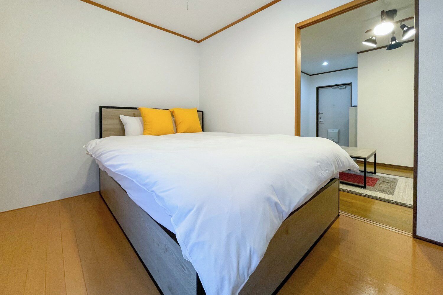 A bedroom with a bed, a mirror, and a wooden floor.