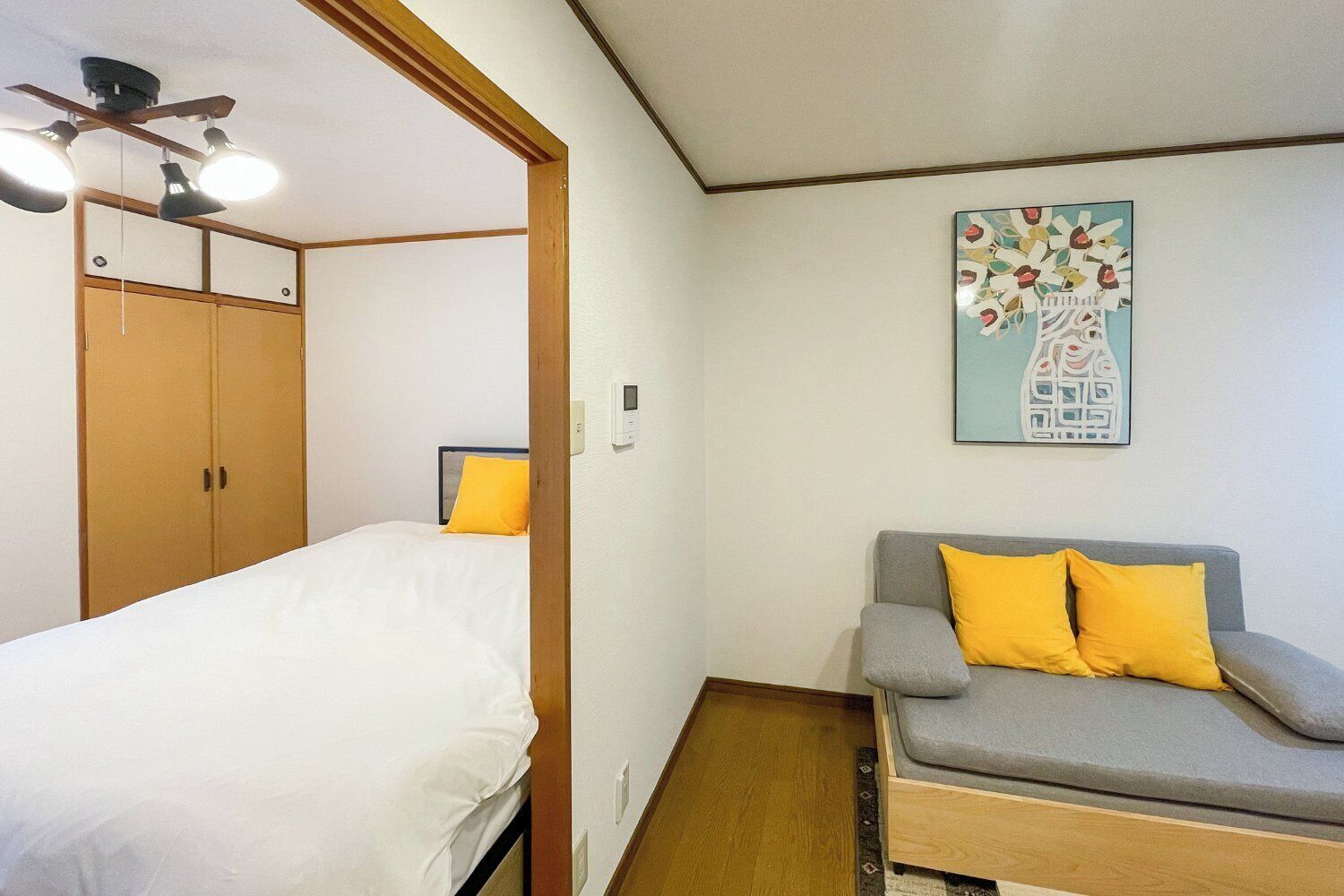A room with a bed, a sofa, a ceiling fan, and a wall-mounted artwork.