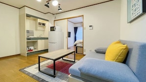 A compact living space with a kitchenette, a sofa with a yellow pillow, and a dining table. - Lavie Heights (Osaka)