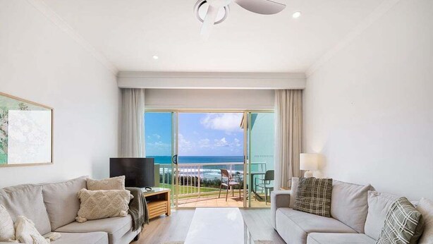 A modern hotel room with a large balcony, a flat-screen TV, two sofas, and a coffee table. - Beachside Stay - Coastal Comfort - Walk to Surf @ Alex Seaside Resort (Sunshine Coast)