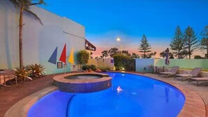 A swimming pool with a tiled edge, lounge chairs, and a flag. - Beachside Stay - Coastal Comfort - Walk to Surf @ Alex Seaside Resort (Sunshine Coast)