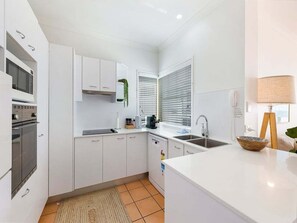 Eine moderne Küche mit weißen Schränken, einem Backofen, einer Spüle und einem Fenster mit Jalousien.