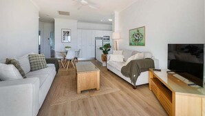 A modern living room with a sofa, coffee table, TV, and a ceiling fan. - Beachside Stay - Coastal Comfort - Walk to Surf @ Alex Seaside Resort (Sunshine Coast)