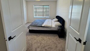 Ein Schlafzimmer mit einem Bett, einem Fenster mit Jalousien, einer Deckenleuchte und einem Teppichboden.