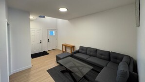 Ein modernes Wohnzimmer mit einem grauen Ecksofa, einem Glastisch und einem Holztisch.