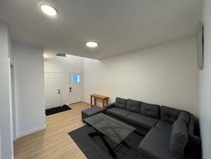 A modern living room with a grey sectional sofa, a glass coffee table, and a wooden side table.