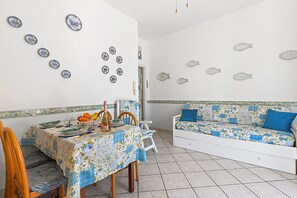 A dining area with a table set for two, a sofa, and wall decorations. - Baia Serena With Terrace & Parking (San Bartolomeo al Mare)