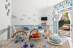 Un comedor con una mesa preparada para dos personas, un frutero y un televisor en la pared.