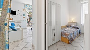 A bedroom with a bed, a wardrobe, a TV, and a bathroom visible through an open door. - Baia Serena With Terrace & Parking (San Bartolomeo al Mare)