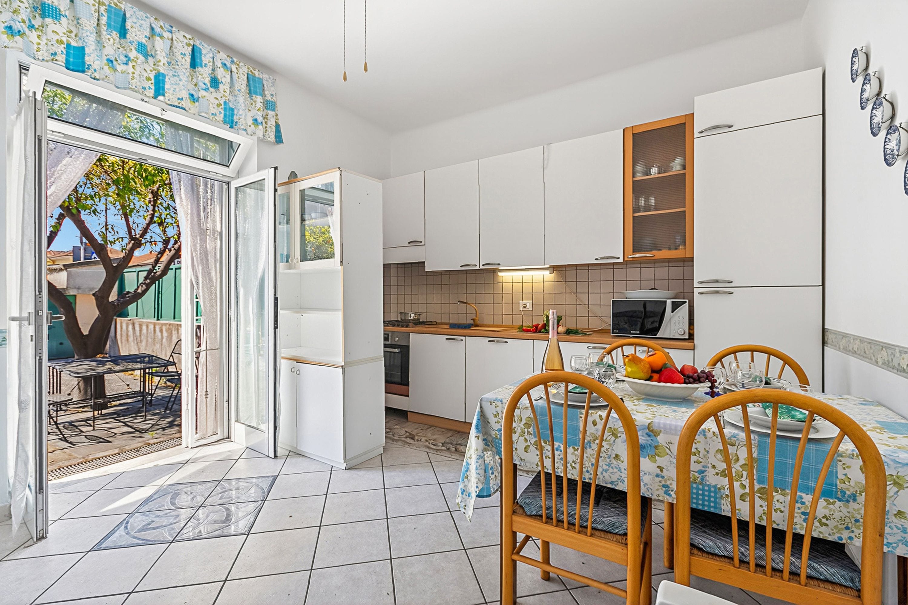A compact kitchen with white cabinets, a dining table with chairs, and a view of the outdoors.