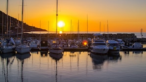 A marina with multiple boats docked, a sunset in the background, and a rocky shoreline. - Baia Serena With Terrace & Parking (San Bartolomeo al Mare)