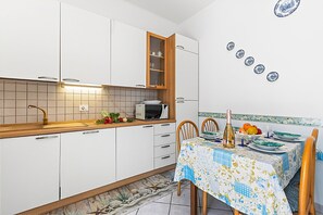 A kitchen with white cabinets, a microwave, and a dining area with a table set for two. - Baia Serena With Terrace & Parking (San Bartolomeo al Mare)