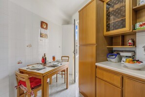 Une cuisine avec des meubles de rangement en bois, une table à manger dressée pour deux personnes et un réfrigérateur.