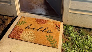 Eine Tür, die zu einem Raum führt, der ein Sofa, einen kleinen Tisch und eine Fußmatte mit dem Schriftzug 'hello' enthält.