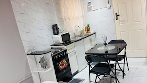 Una cocina compacta con microondas, estufa y lavaplatos, una mesa de comedor con sillas y una puerta.