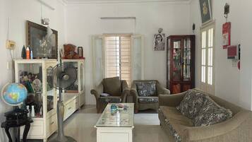 A living room with a sofa, armchair, a small table, a globe, a fan, and a cabinet with various items.