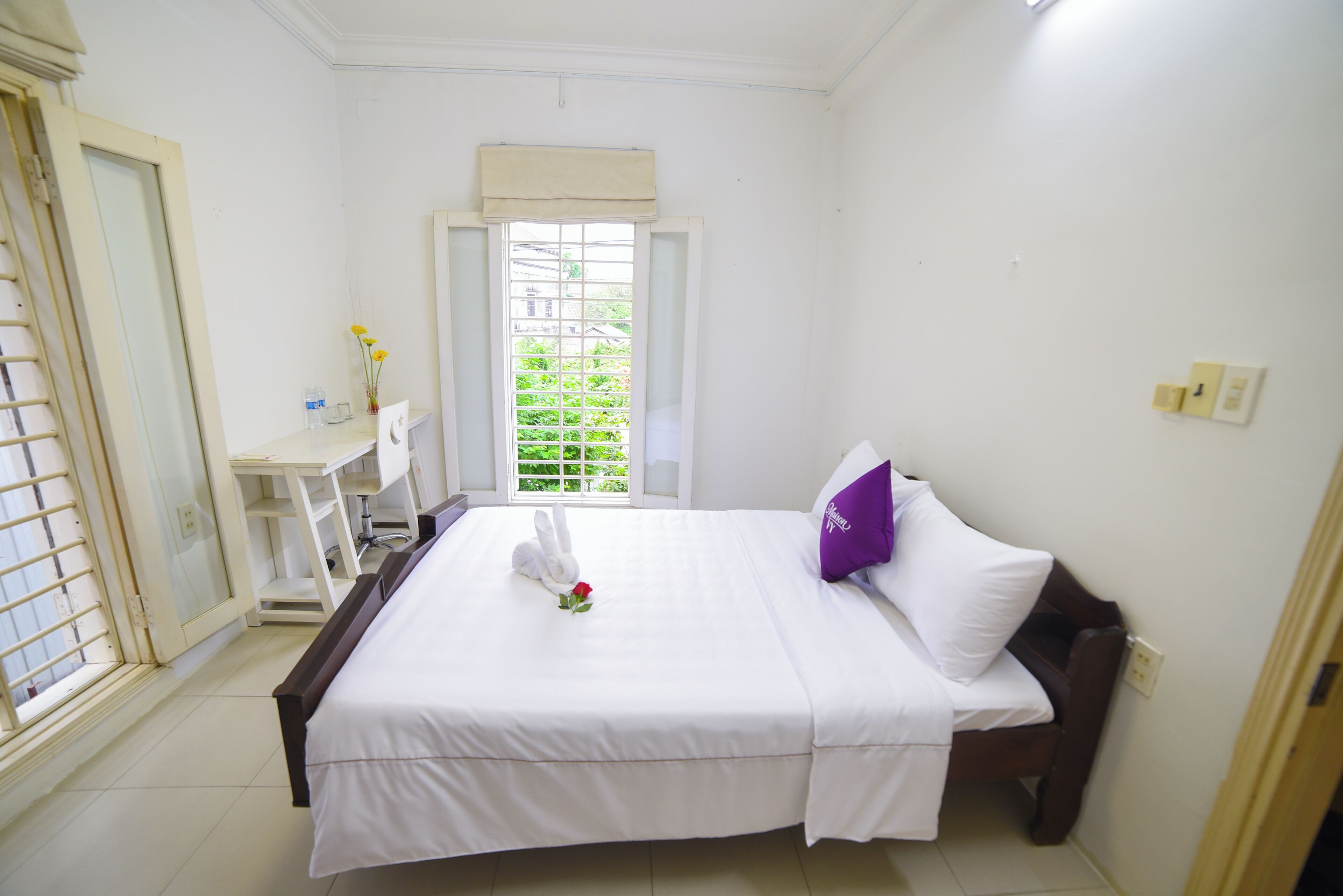 Une chambre d’hôtel avec un lit, un bureau, une chaise, une fenêtre donnant sur un paysage agréable et une porte.