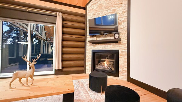 A modern living room with a fireplace, a mounted television, and a wooden table with a deer sculpture.