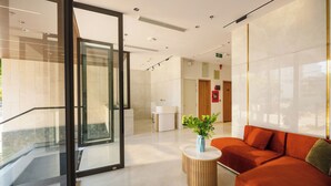 En moderne lobby med glas elevator, reception og siddeområde med plante.