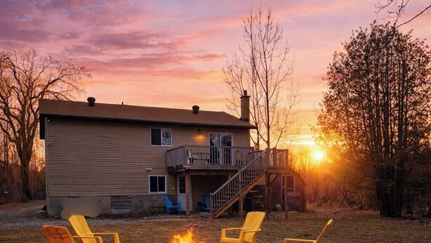 A house with a fire pit and chairs in the yard.