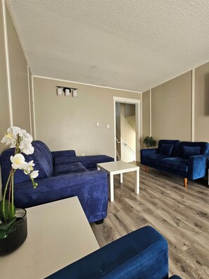 Een woonkamer met een blauwe bank, een witte salontafel en een potplant.