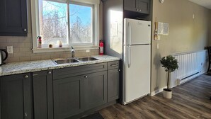 A kitchen with dark cabinets, a white refrigerator, a window with a view of trees, and a small potted plant.
