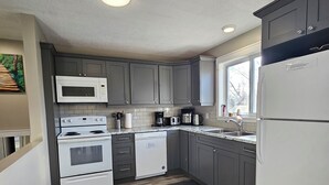 A modern kitchen with grey cabinets, a white microwave, stove, dishwasher, and refrigerator.