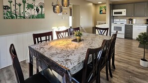 A dining area with a table covered in a patterned tablecloth, surrounded by chairs, and a ceiling light fixture above.
