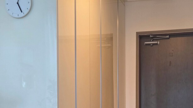 En hall med en klocka, en glasvägg och en dörr.