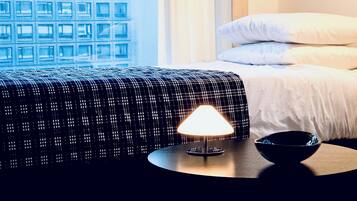 A hotel room with a bed, a bedside table with a lamp, a bowl, and a window with a view of a building.