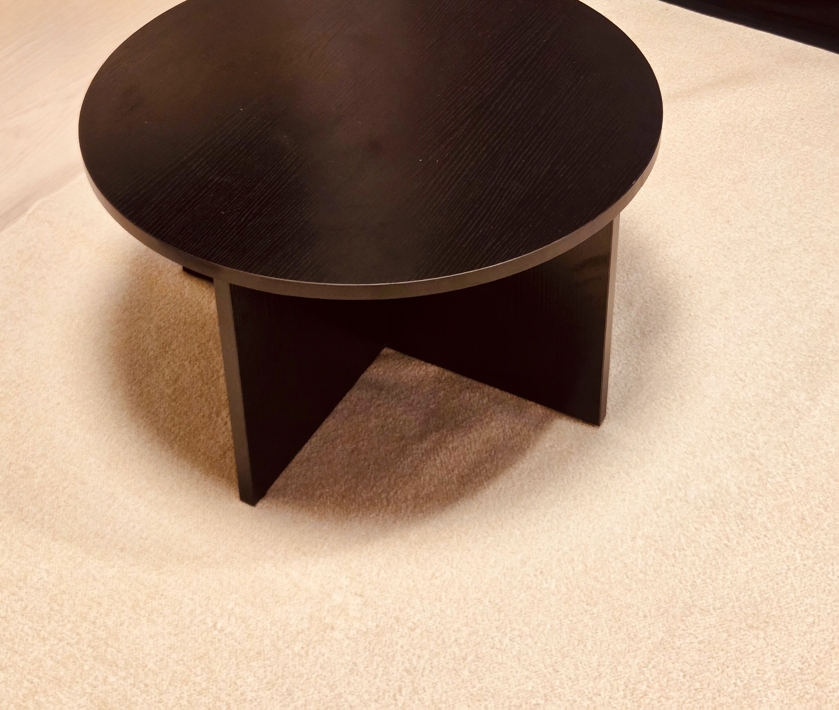 A round, black table with a simple, modern design on a carpeted floor.
