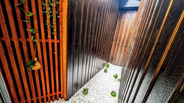 A narrow pathway flanked by vertical wooden slats, with small plants at the base. - The Dream Stays ShinSekai (Osaka)